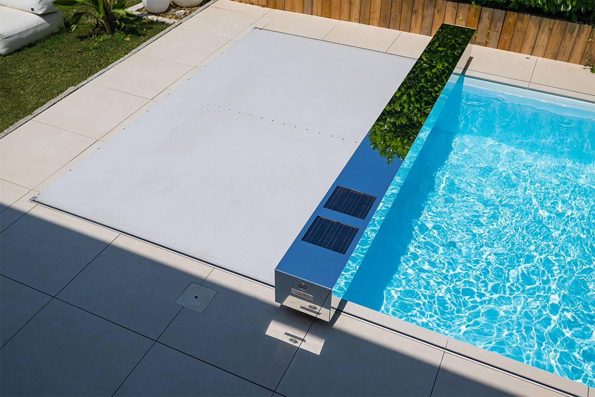 Piscine moderne recouverte d’une couverture Coverseal beige, avec habillage effet miroir équipé de panneaux solaires, intégrée dans une terrasse carrelée.