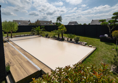 DreamHomeFamily4 Piscine totalement sécurisée grâce à une couverture Coverseal beige, intégrée dans un jardin paysager avec végétation méditerranéenne.